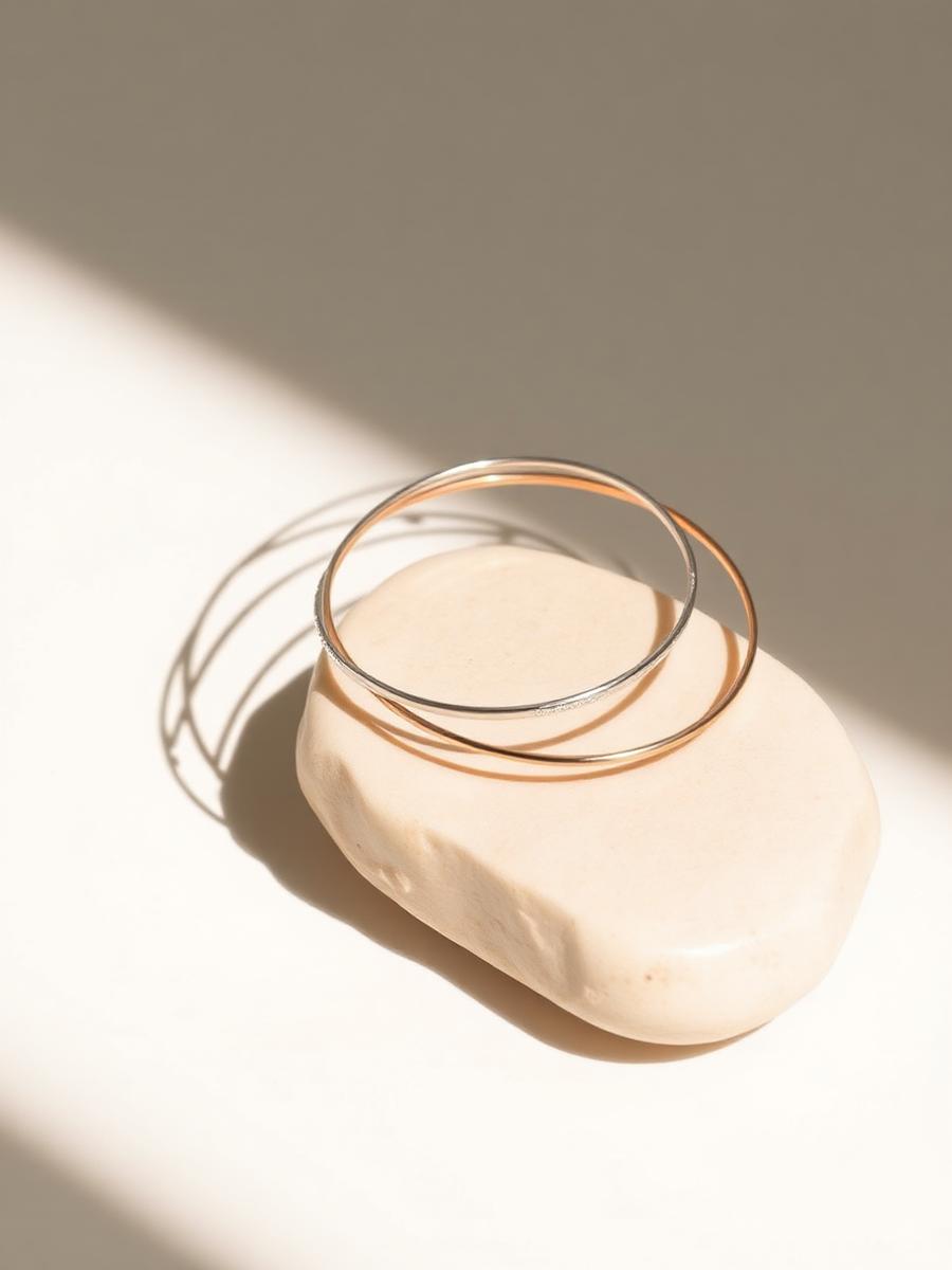 Slim silver and rose finish bangles resting on an ivory pebble